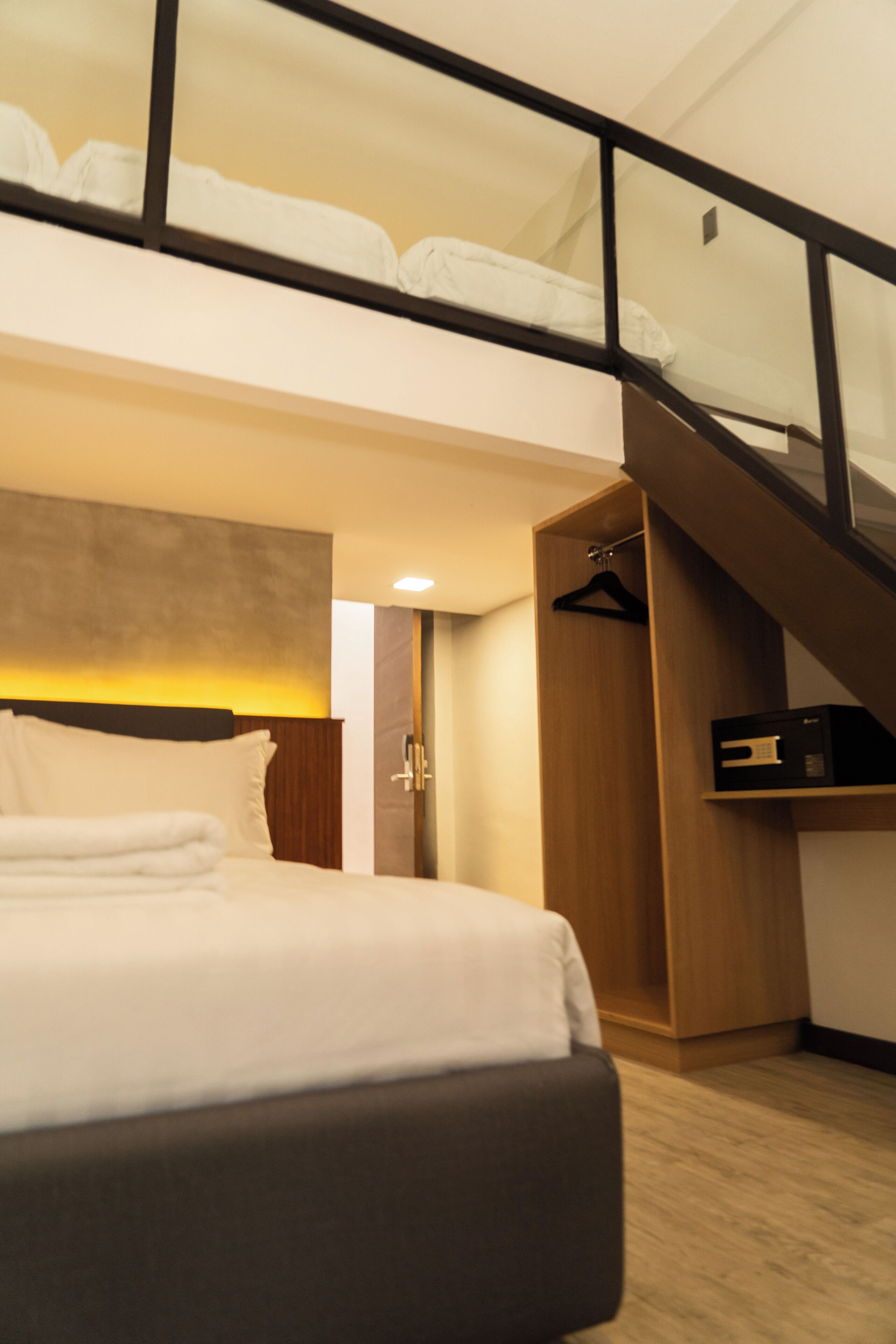 A modern hotel room with a large bed, a wooden wardrobe, a coat rack, and a staircase leading to an upper level.