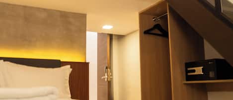 Une chambre d’hôtel moderne avec un grand lit, une armoire en bois, un porte-manteau et un escalier menant à un niveau supérieur.