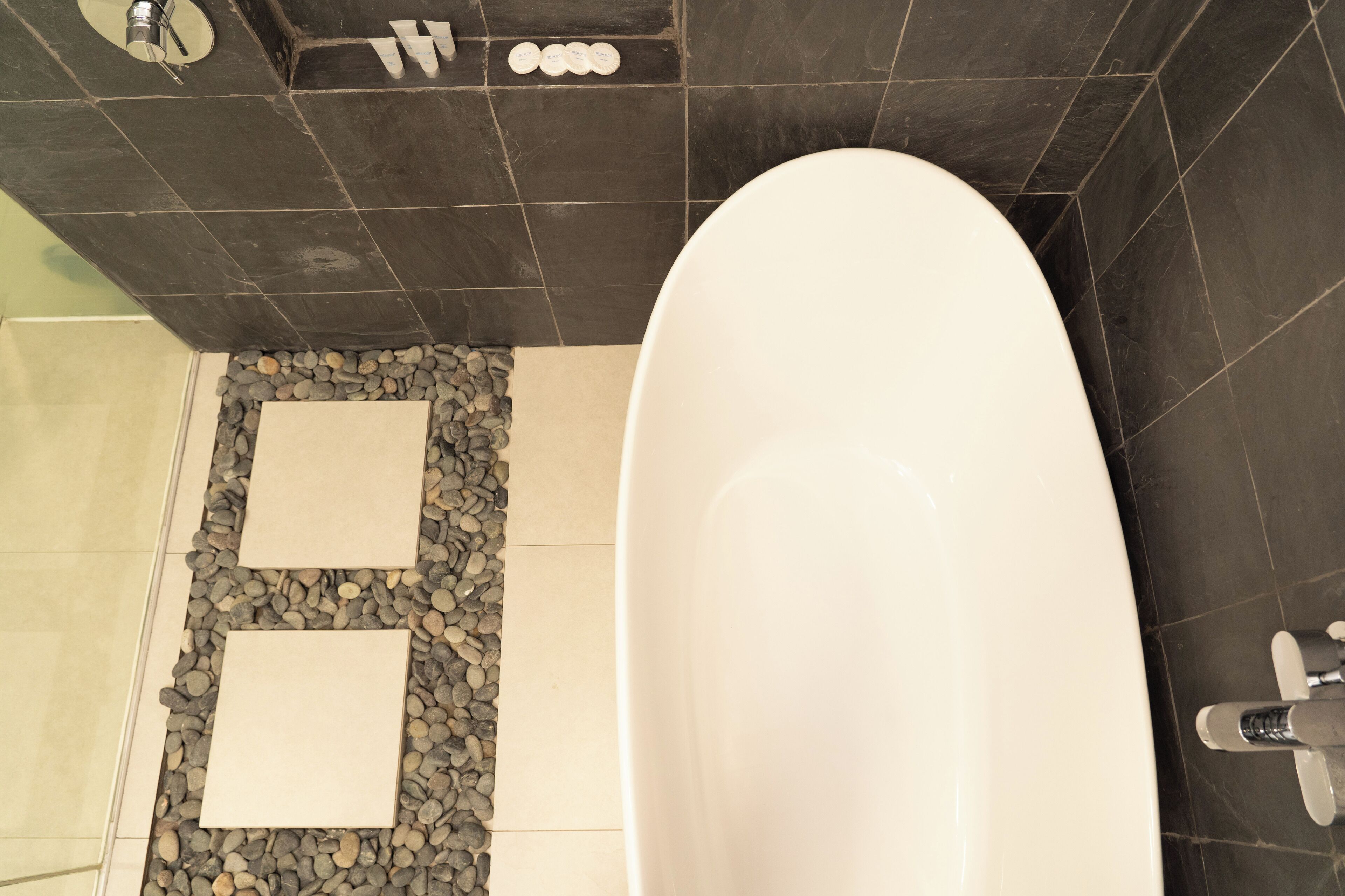 A modern bathroom with a freestanding bathtub, a built-in shelf with toiletries, and a pebble-patterned floor.