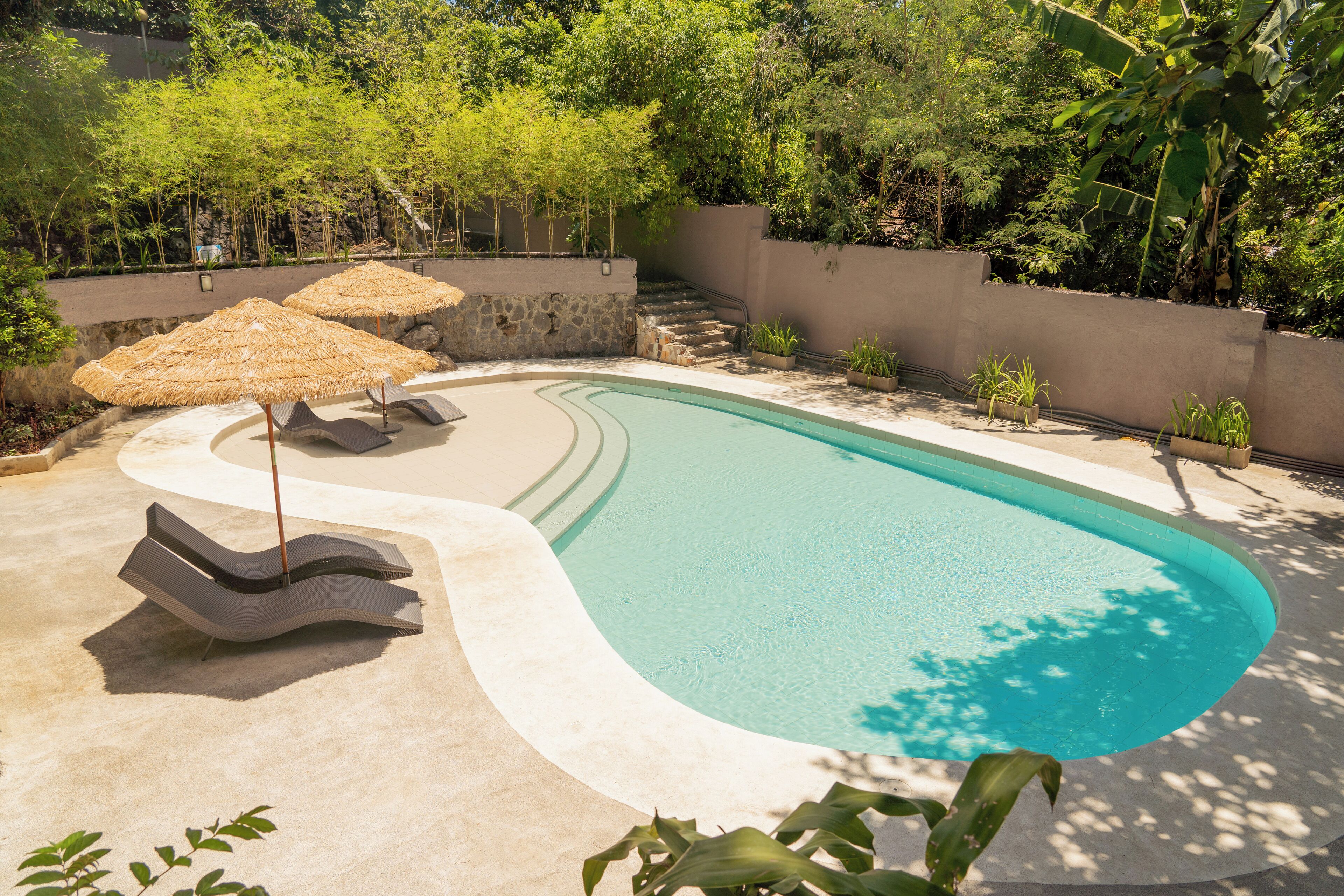 A swimming pool with a curved edge, surrounded by a stone wall and lush greenery.