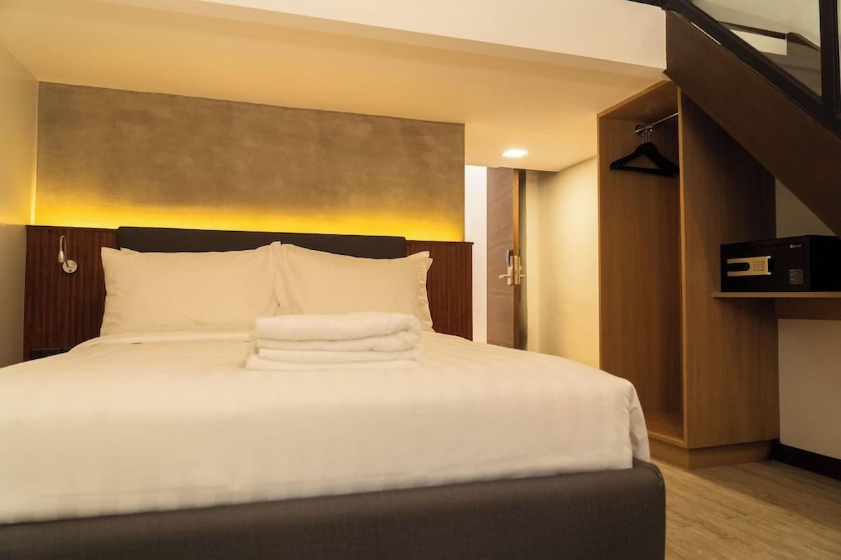A modern hotel room with a large bed, a wooden headboard, a built-in wardrobe, and a staircase.