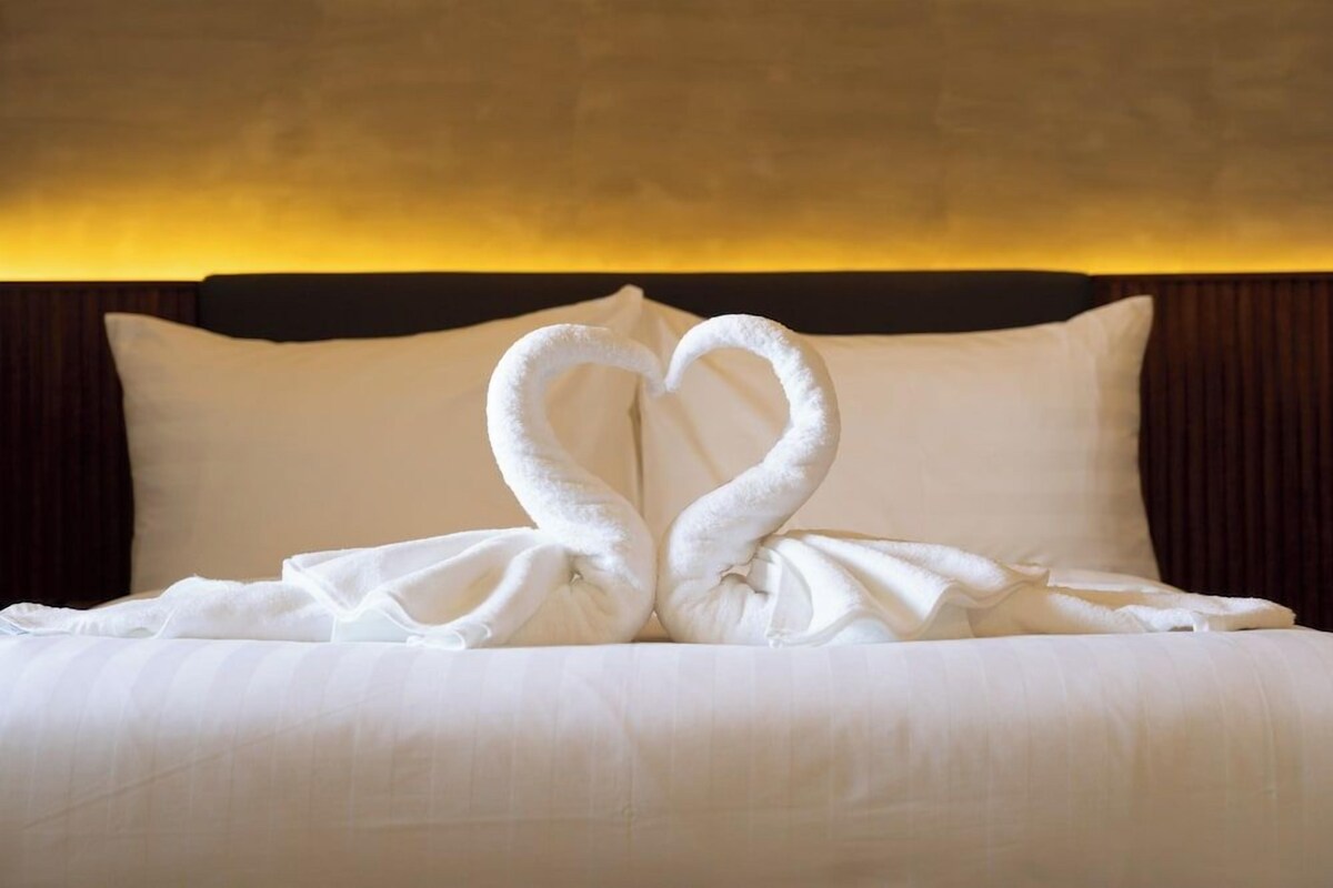 Un lit avec du linge de lit blanc et deux serviettes disposées en forme de cœur.