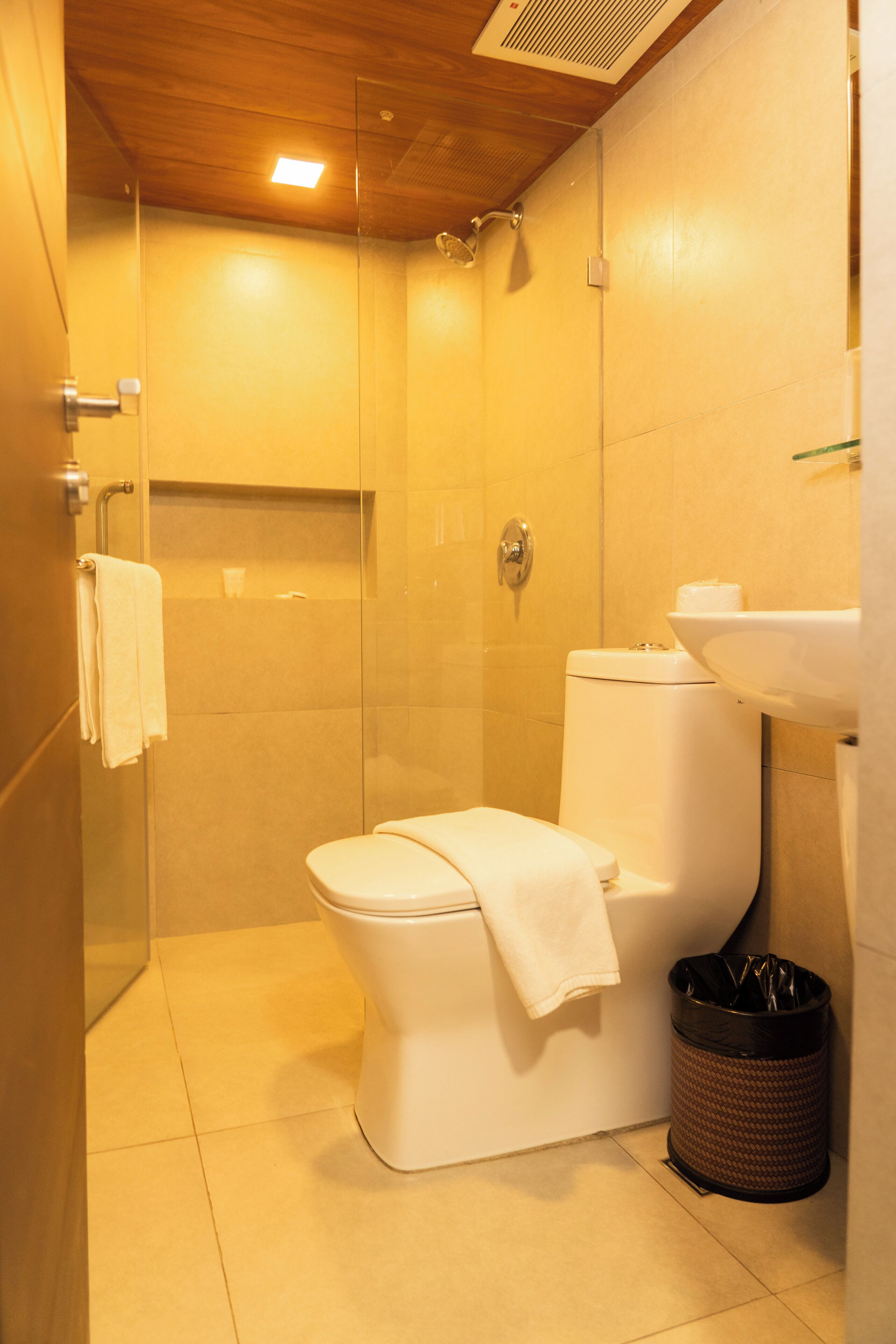 Une salle de bain comprenant des toilettes, une douche fermée par une paroi de verre, un lavabo et une poubelle.