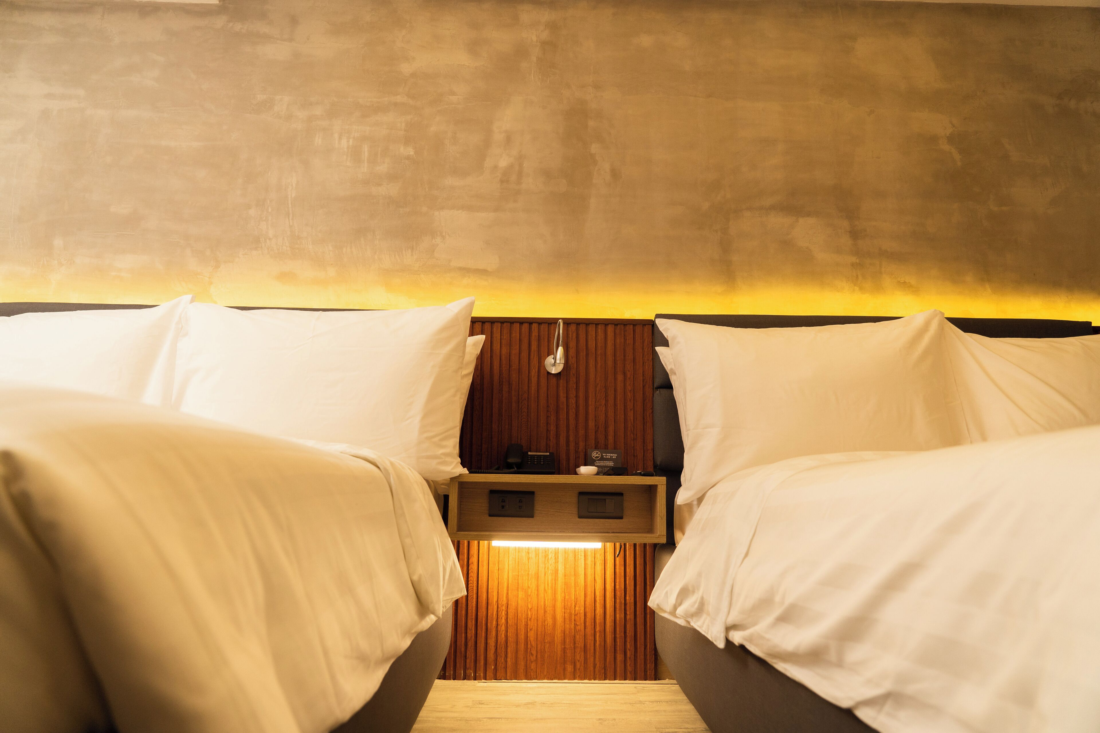 A room with two beds, a wooden headboard, and a small bedside table with a lamp.