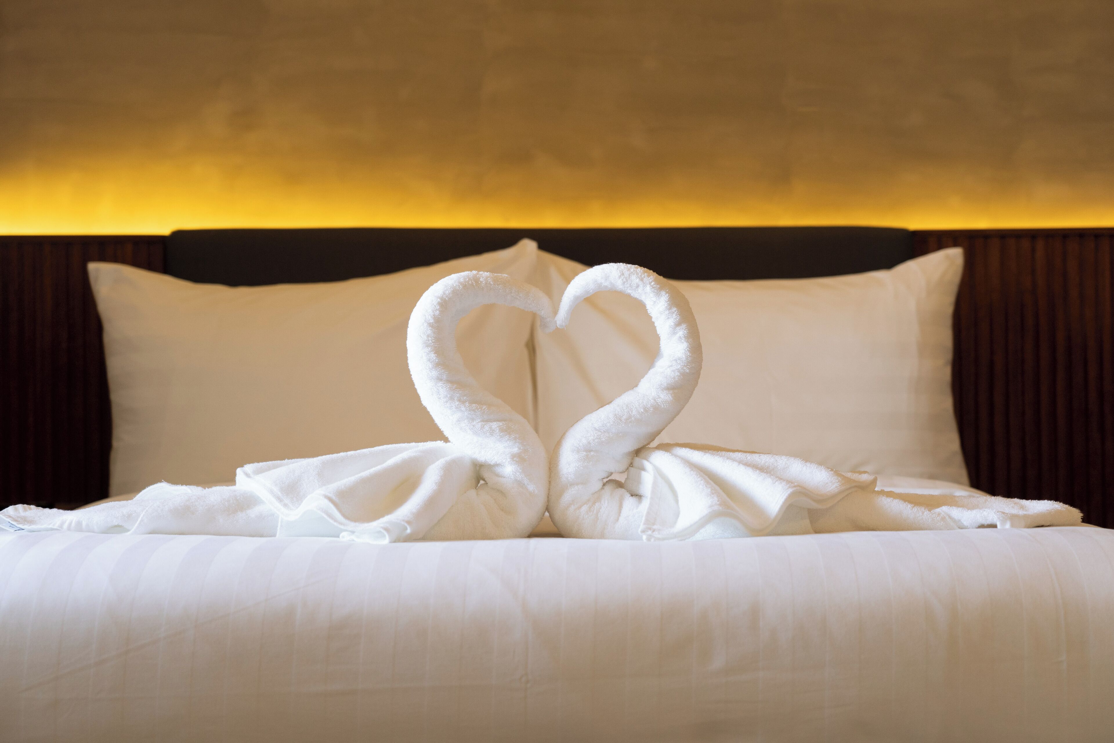 Een bed met witte lakens en twee handdoeken gevouwen in de vorm van een hart.