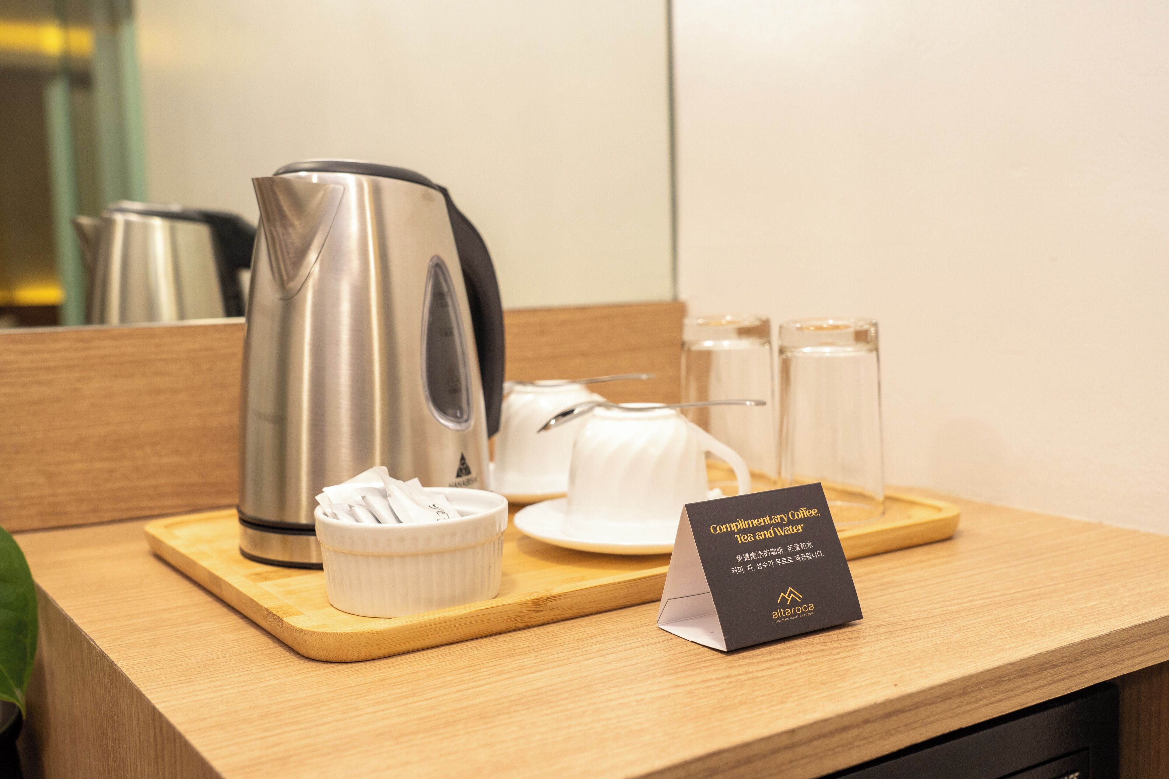 A coffee station with a coffee pot, cups, and a sign indicating complimentary coffee, tea, and water.