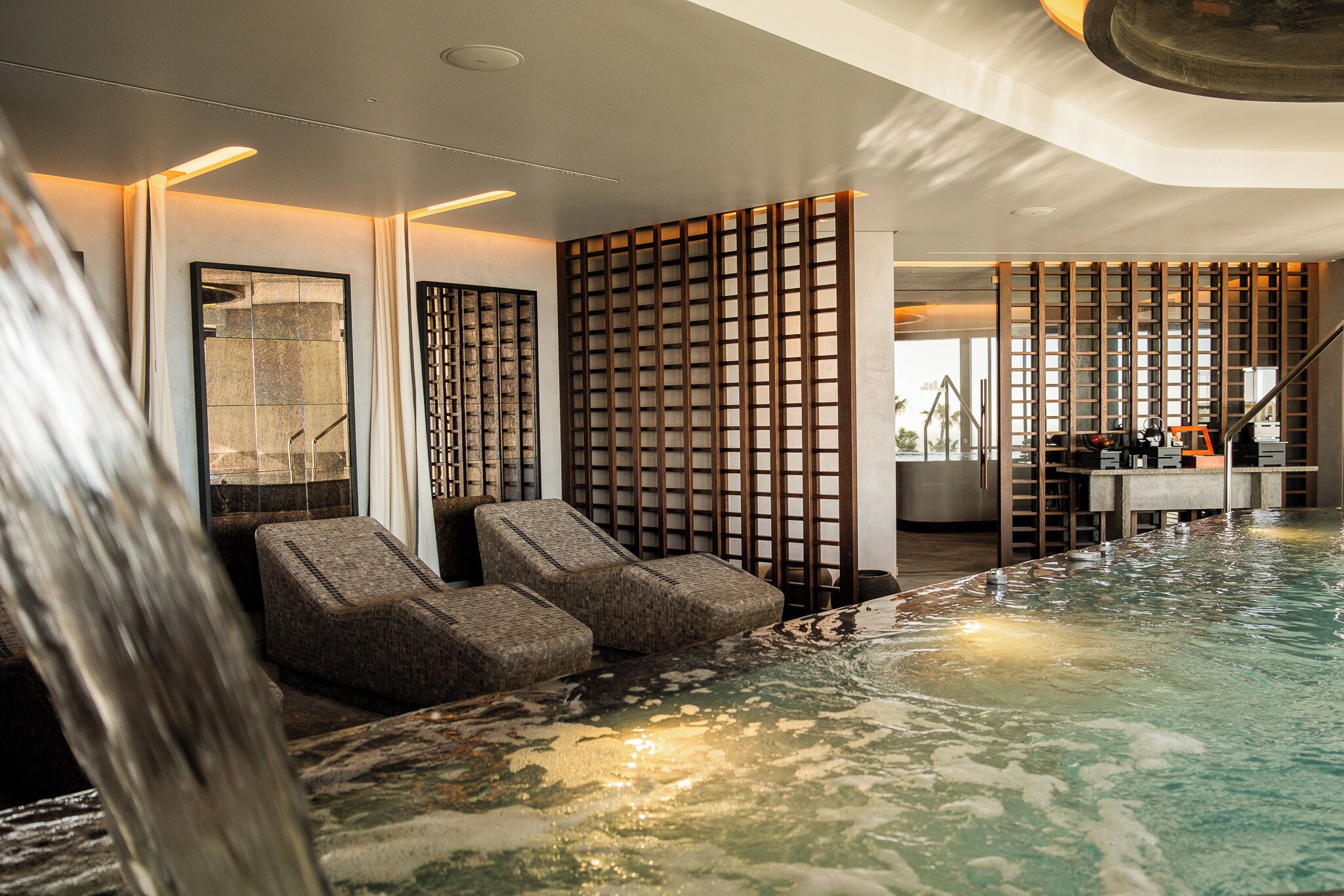Et spa-område med jacuzzi, siddepladser og et vandfald.