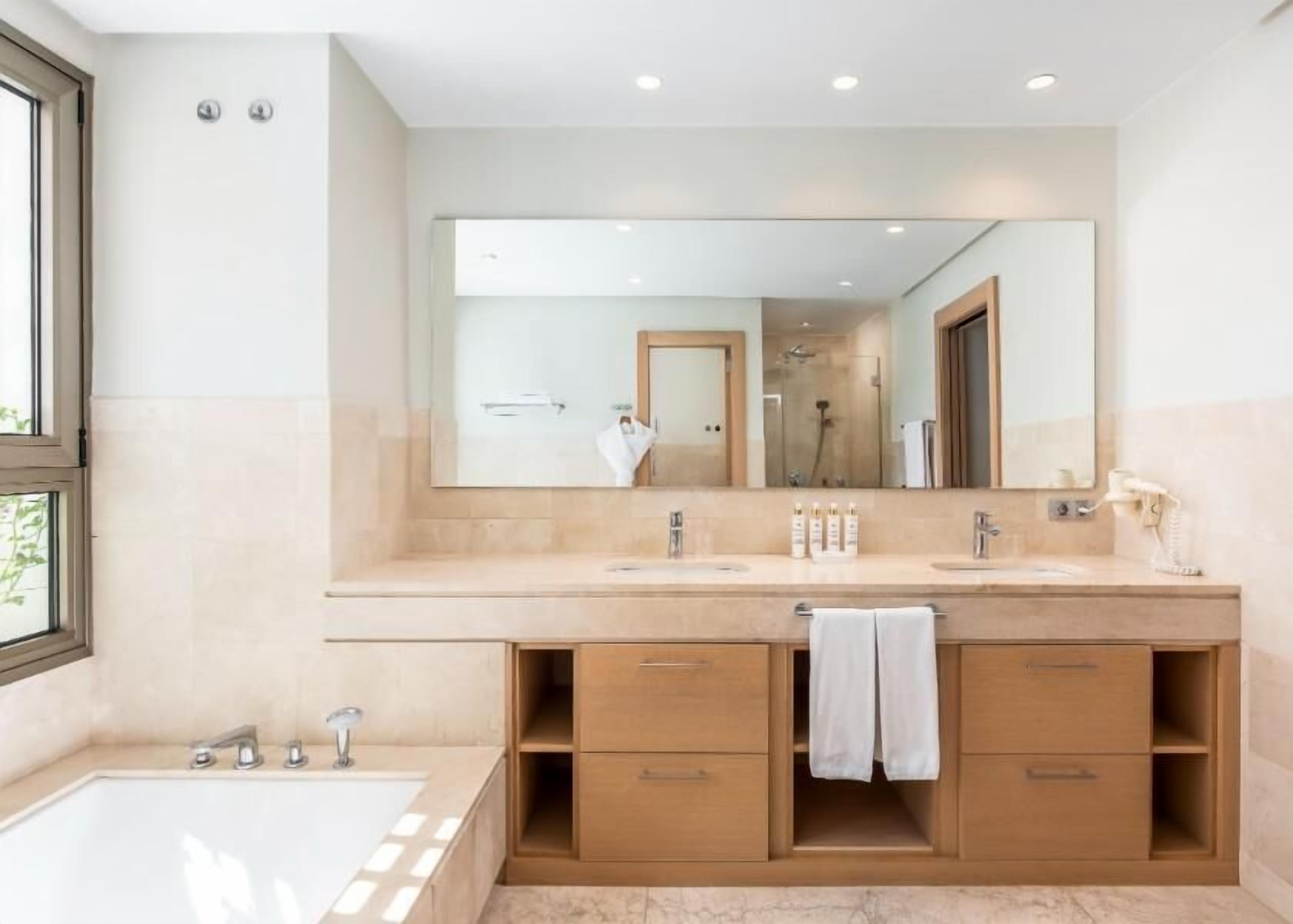 Ein modernes Badezimmer mit einem großen Spiegel, zwei Waschbecken, einer Badewanne und Holzschränken.