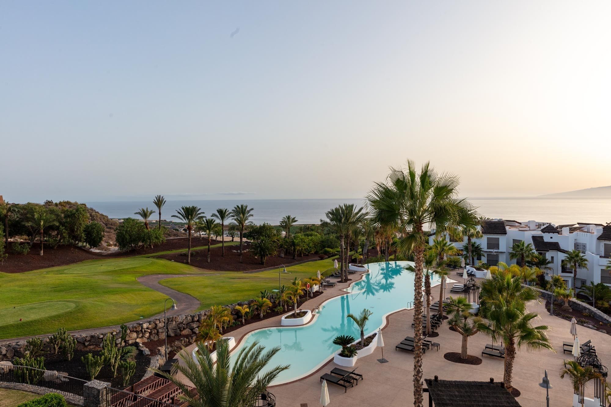 Un resort con una amplia piscina, palmeras y vista al océano.