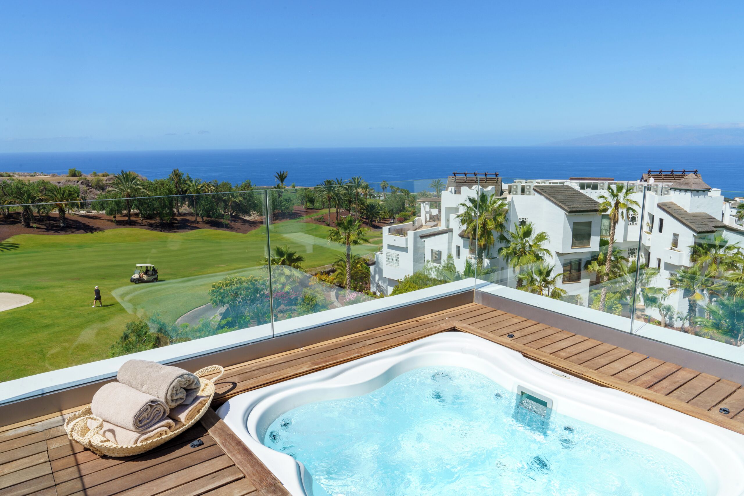 A hot tub on a wooden deck with a view of a golf course and ocean.