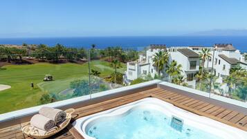 A hot tub on a wooden deck with a view of a golf course and ocean.