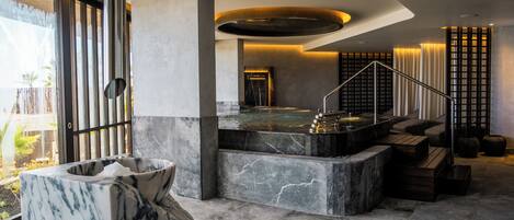 Un espace spa moderne doté d’un bassin en marbre, d’un jacuzzi et d’un escalier menant à une salle privée.