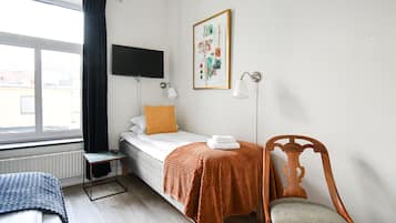 Un dormitorio pequeño y ordenado con una cama individual, una silla, una mesa y un televisor montado en la pared.