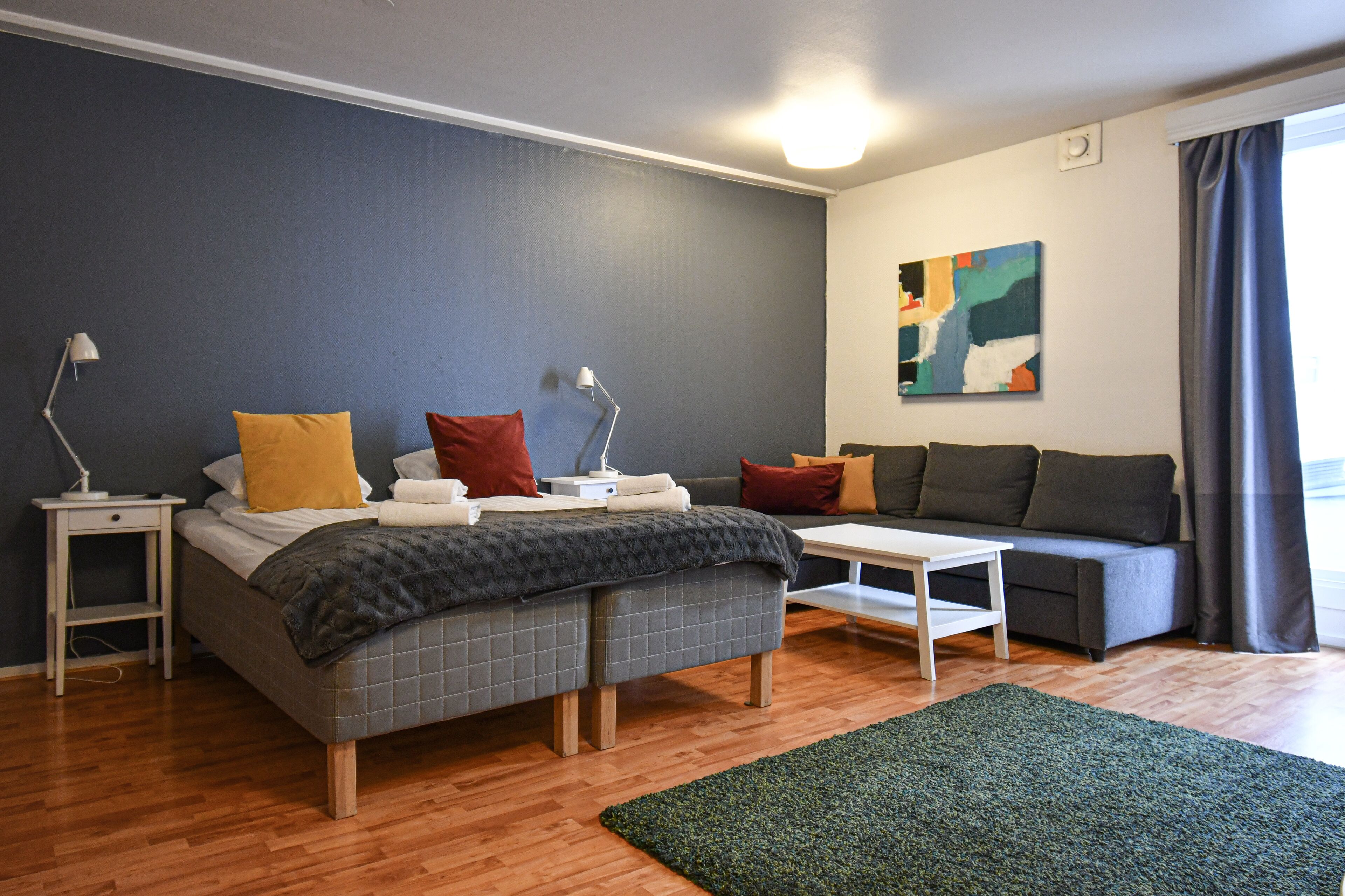 Un dormitorio moderno con una cama, mesitas de noche, un sofá y un cuadro en la pared.