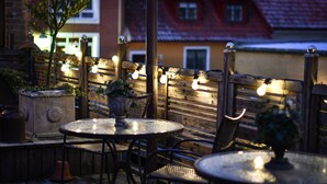 Un patio al aire libre con mesas y sillas redondas, luces colgantes y plantas en macetas.