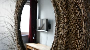 A circular woven mirror with a visible reflection of a room interior, including a wooden table and a television.