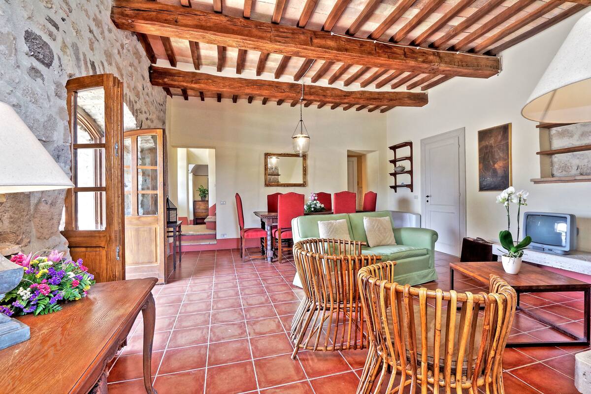 Un intérieur rustique avec un plafond en bois, un sol carrelé, des chaises en osier, un canapé vert et un téléviseur.