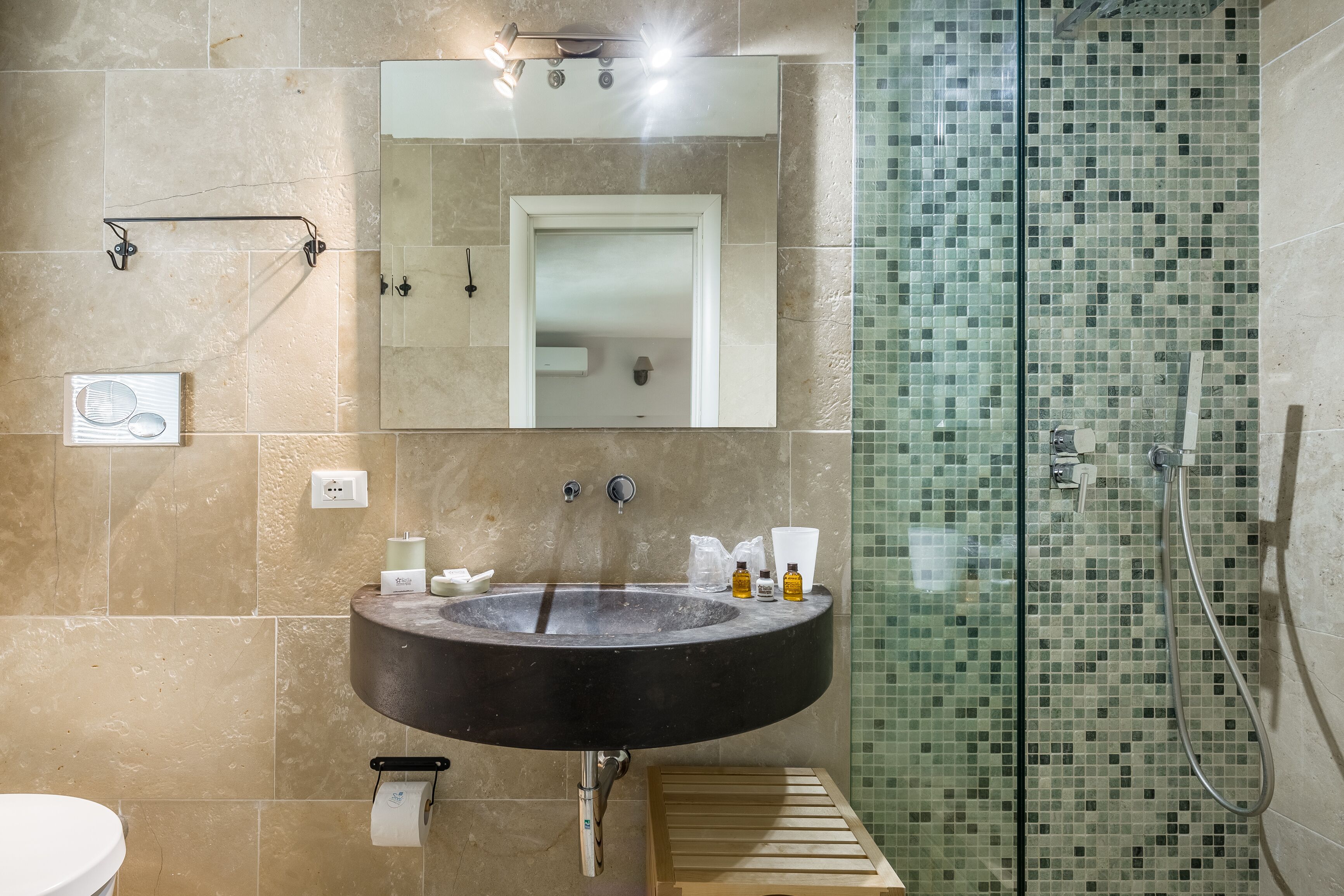 A bathroom with a large black sink, a mirror, a shower with a glass door, and beige tiled walls.