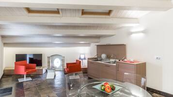 Un salon moderne avec une table en verre, des fauteuils rouges, un téléviseur à écran plat et un coin cuisine doté de meubles en bois et d’un évier.