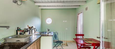 Een keuken met een spoelbak, fornuis en een raam. Er is een eethoek met een tafel en stoelen.