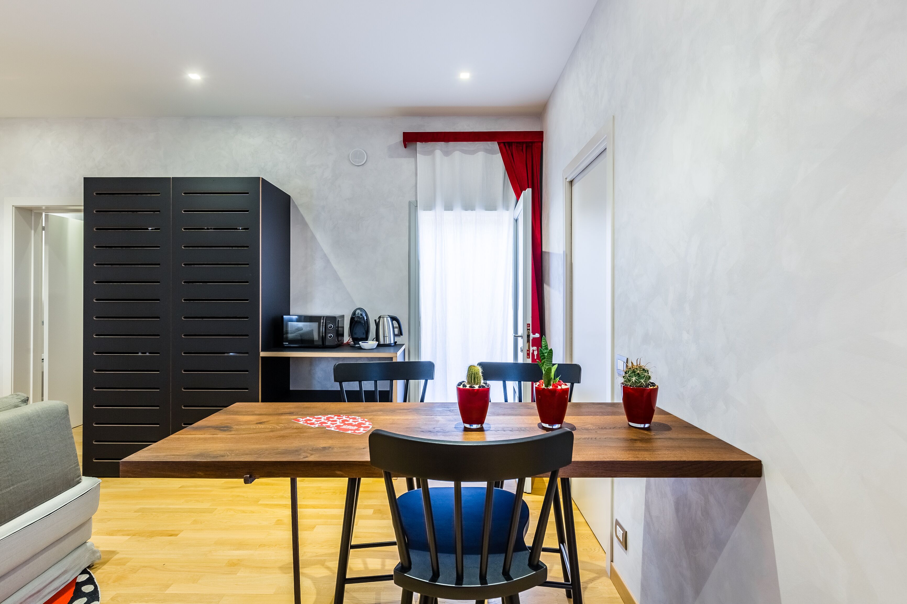 A compact living space with a dining area featuring a wooden table, blue chairs, and red potted plants.
