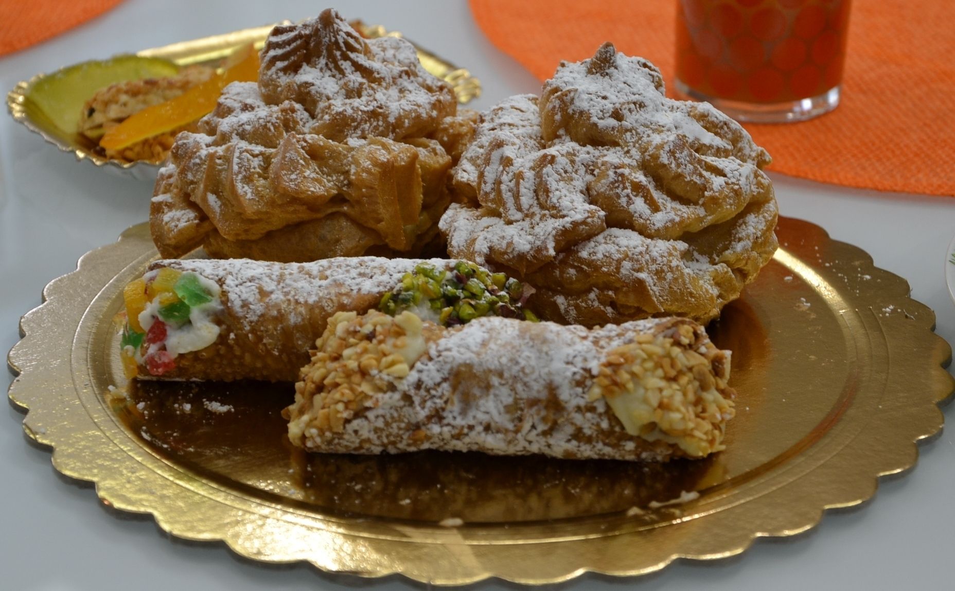 A variety of pastries on a golden plate, including a rolled pastry with colorful filling and a dusting of powdered sugar.