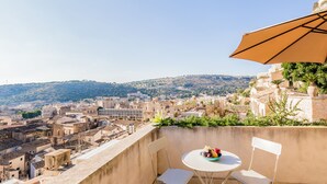 A balcony with a table and chairs, overlooking a cityscape with historic buildings and a hill in the distance.