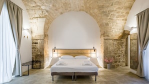 A bedroom with a stone arch ceiling, a bed with white linens, and two bedside tables with lamps.