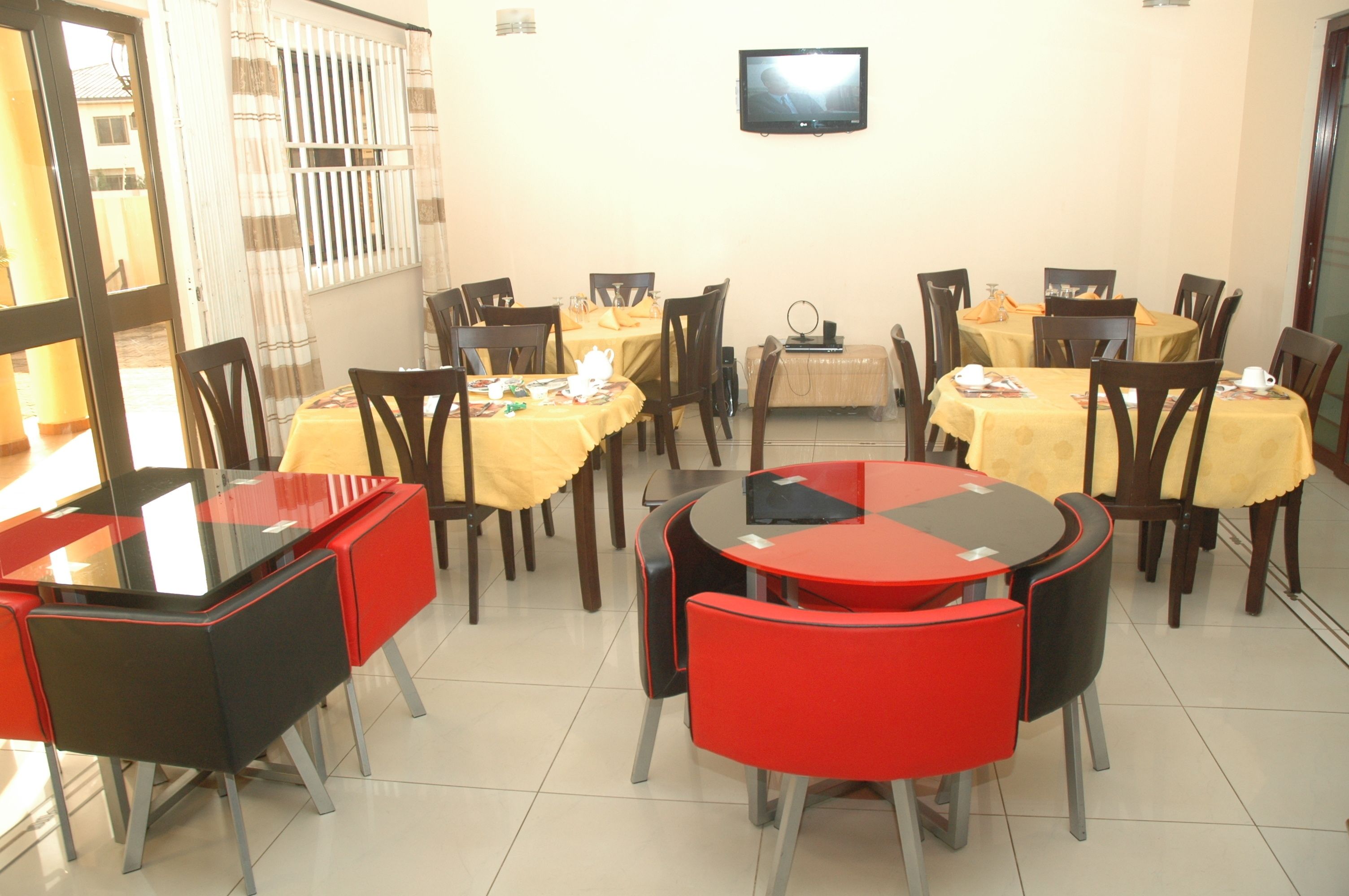 A dining area with multiple tables and chairs, a television on the wall, and a window with blinds.
