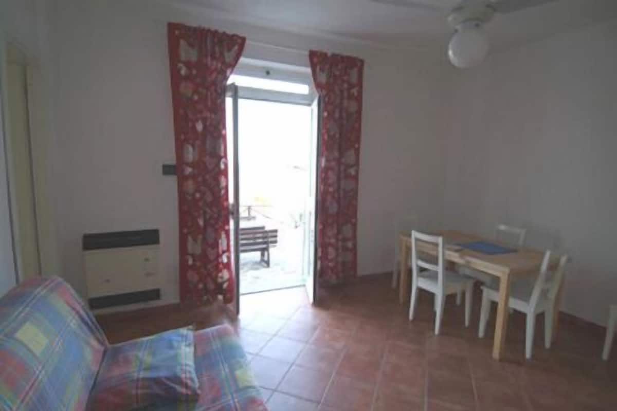 A room with a sofa, a small table with chairs, and a window with red curtains.