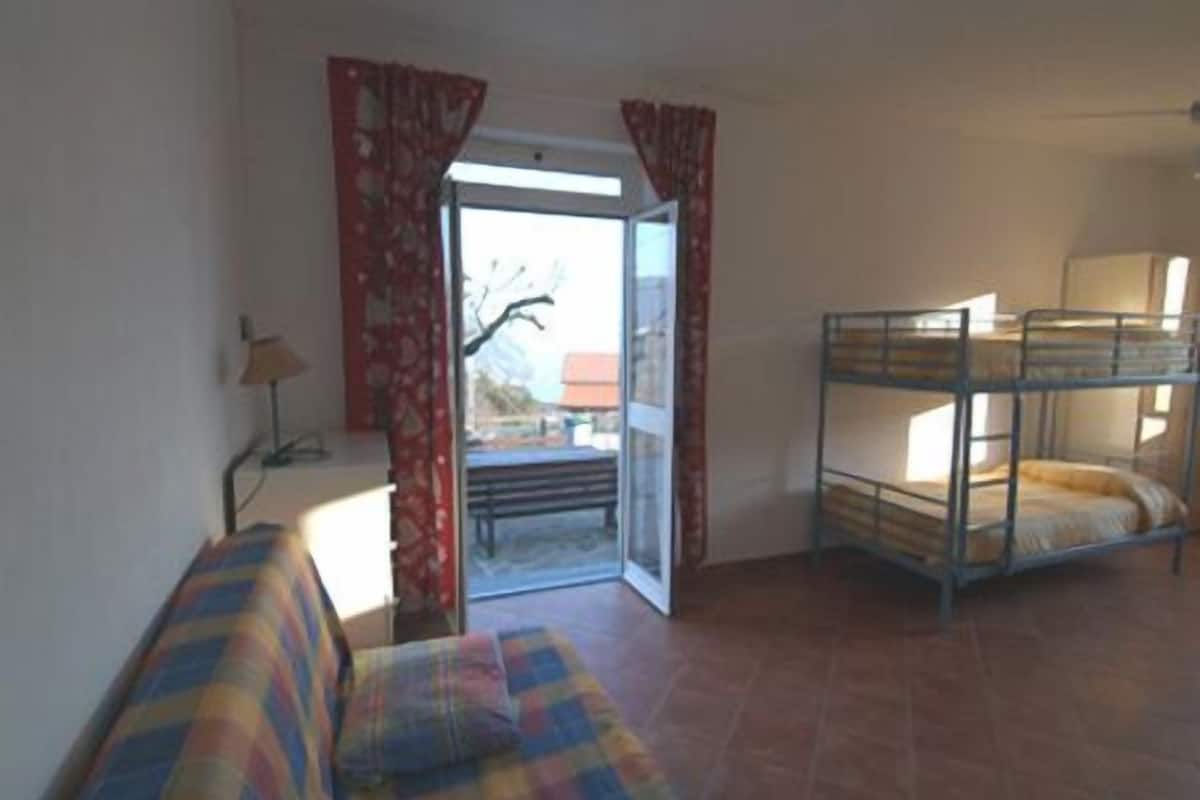 A room with a bunk bed, a sofa, a lamp, and a window with curtains.