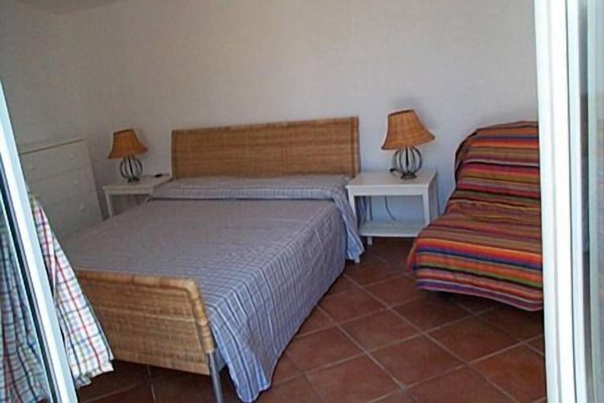 A bedroom with a bed, two bedside tables, a chair, and a colorful striped blanket.