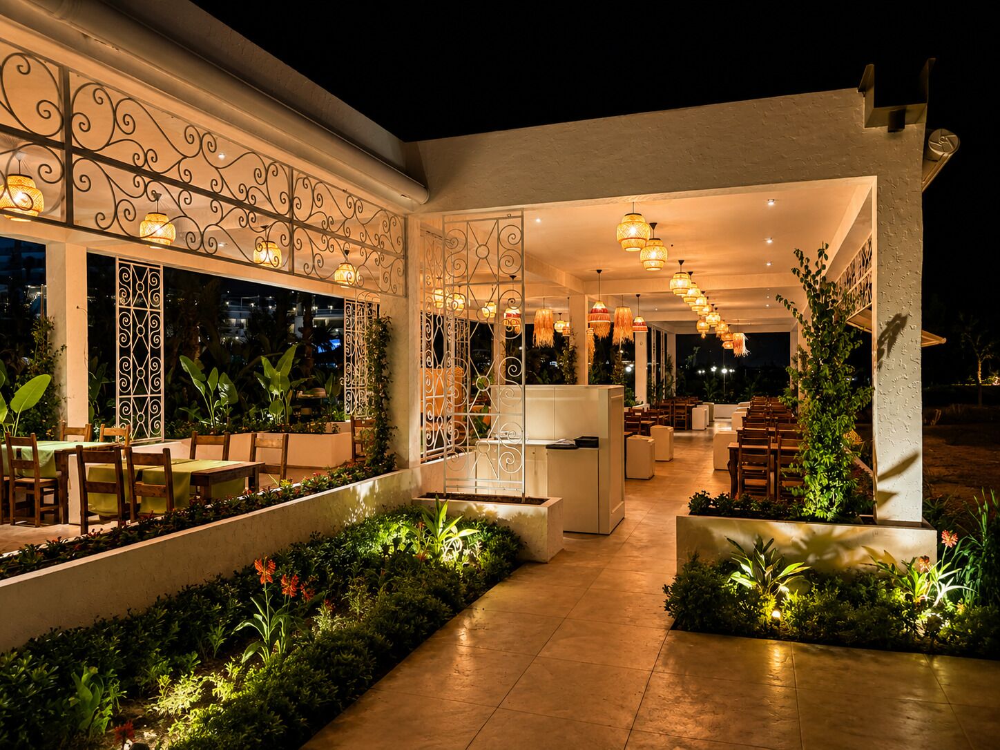 An outdoor dining area with tables and chairs, decorative metal railings, and potted plants.