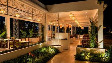 An outdoor dining area with tables and chairs, decorative metal railings, and potted plants.