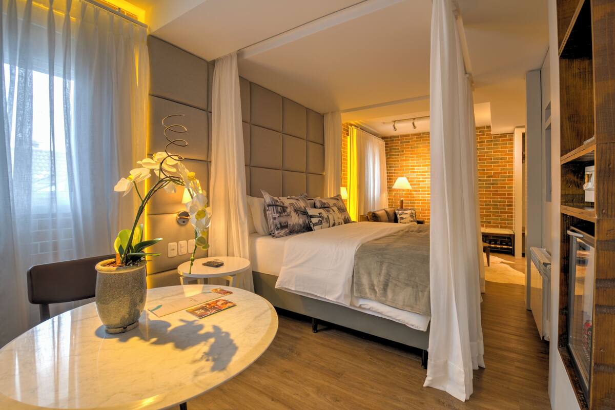 A hotel room with a bed, a small table with a plant, a chair, and a view of the Eiffel Tower through the window.