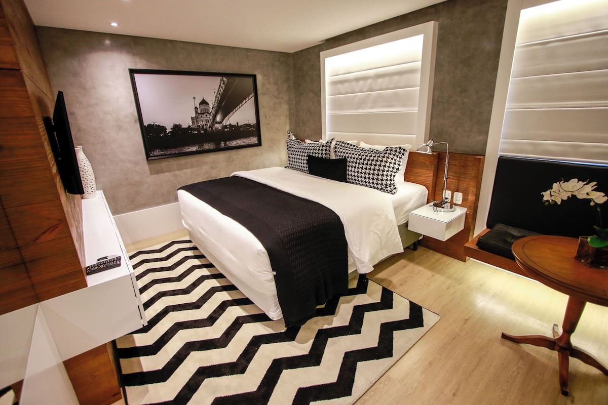 A modern bedroom with a large bed, a flat-screen TV, a framed picture on the wall, and a wooden nightstand.