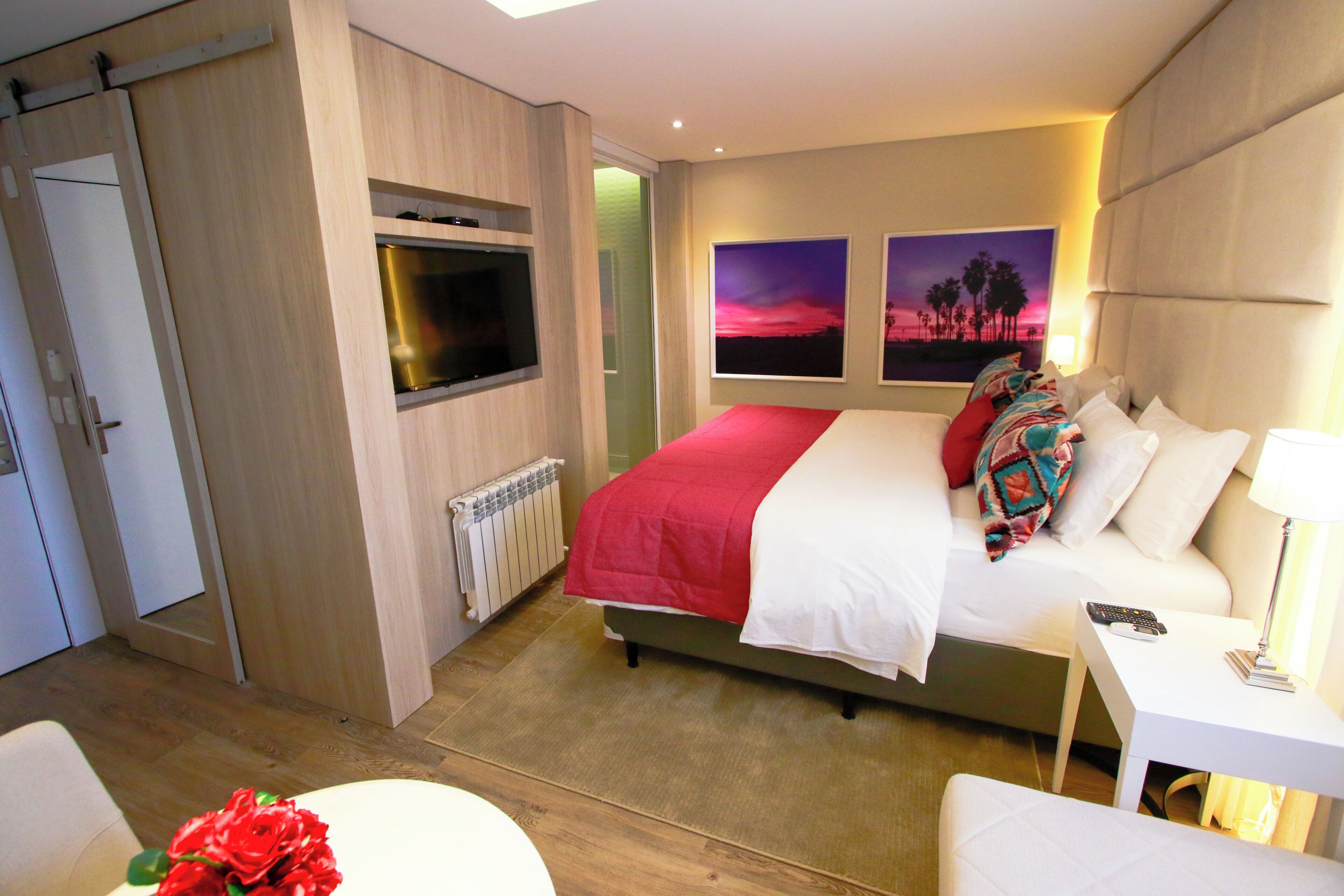 A modern hotel room with a large bed, a TV mounted on the wall, and two framed pictures on the wall.