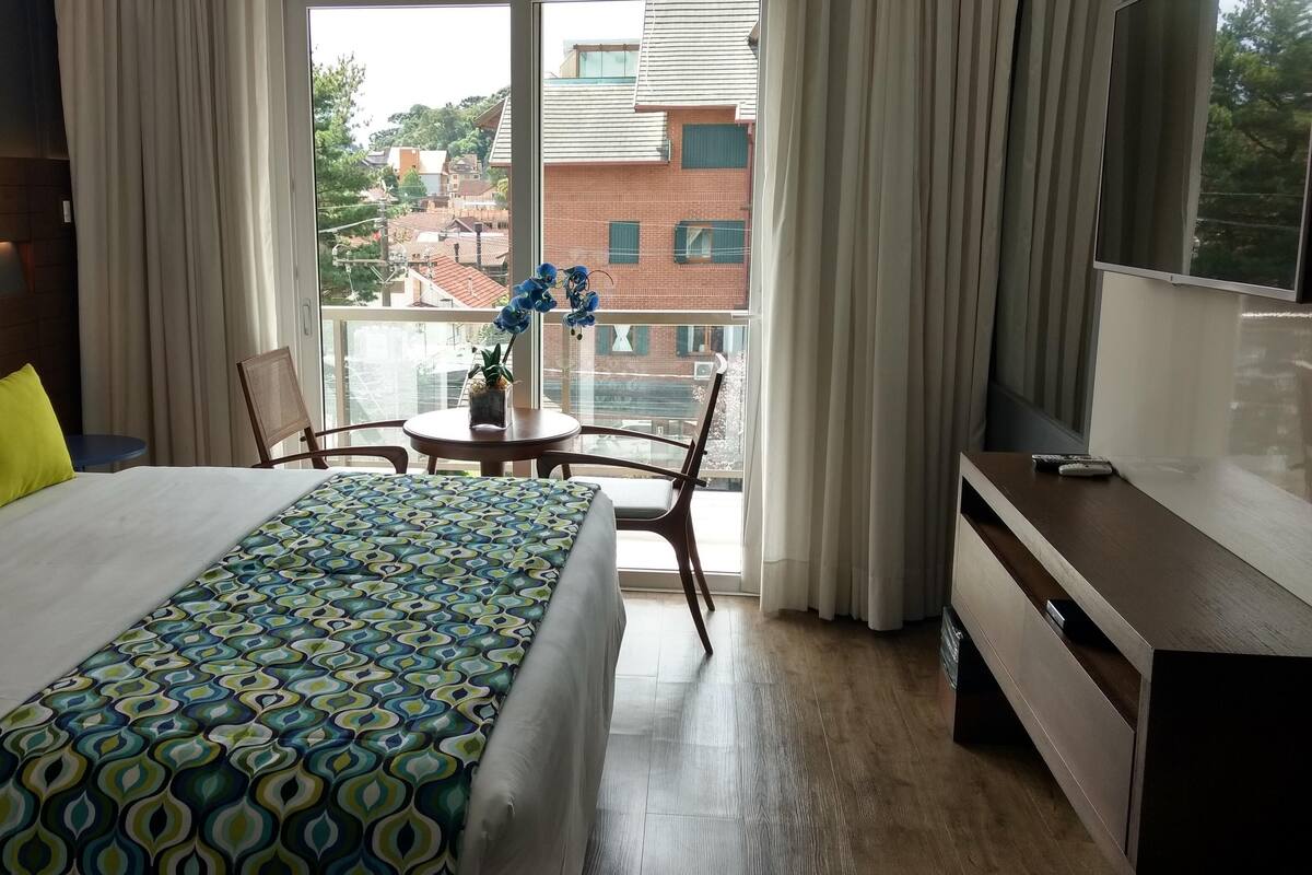 A hotel room with a bed, a desk, a chair, and a view of the cityscape.