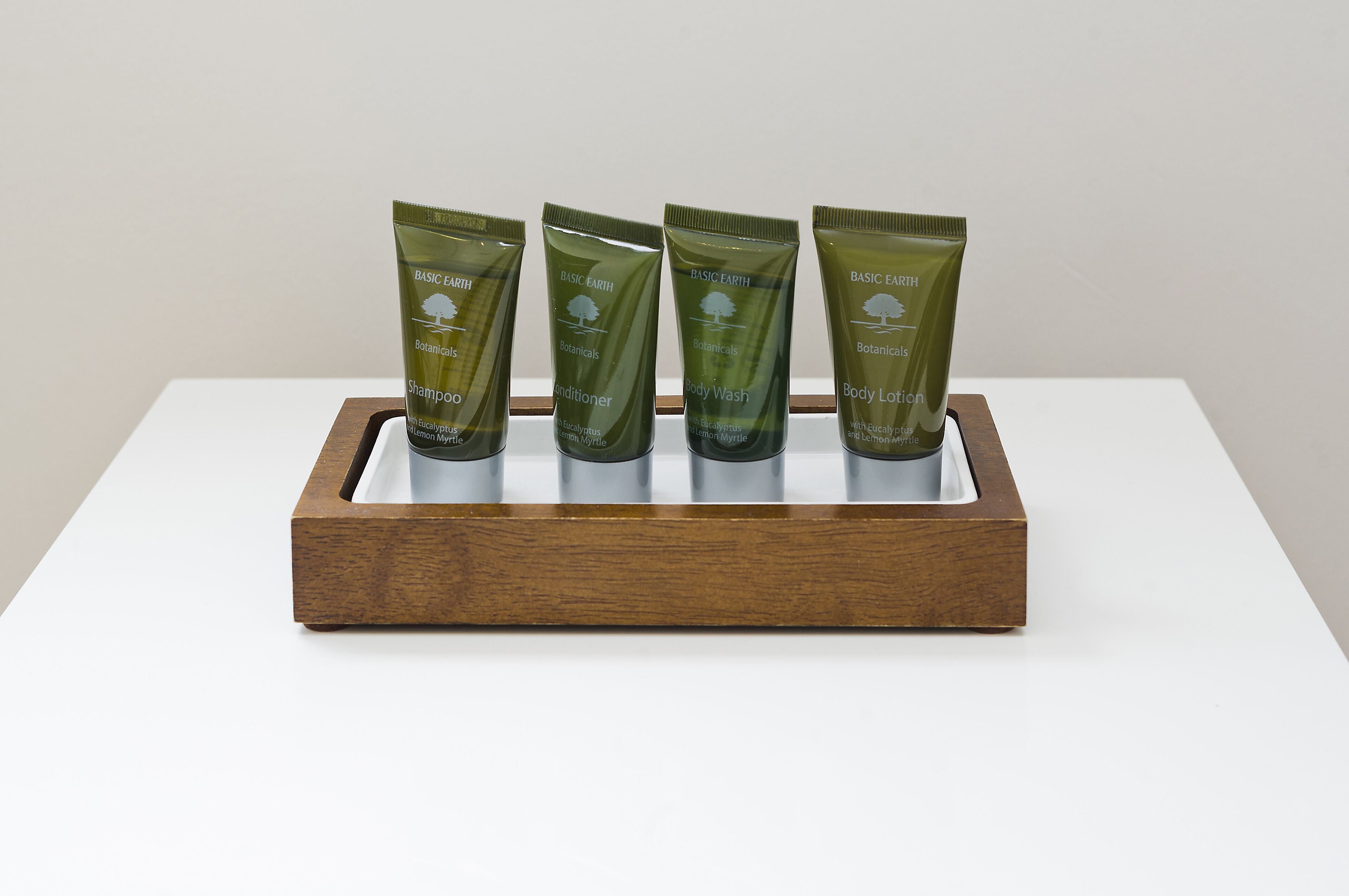 Four green tubes of Basic Earth products on a wooden tray.
