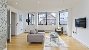 A modern living room with a grey sofa, a coffee table, and a TV mounted on the wall. - Red Lion Court by City2Stay (London)