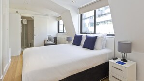 A modern hotel room with a large bed, bedside table, lamp, and a view of the city through the window. - Red Lion Court by City2Stay (London)