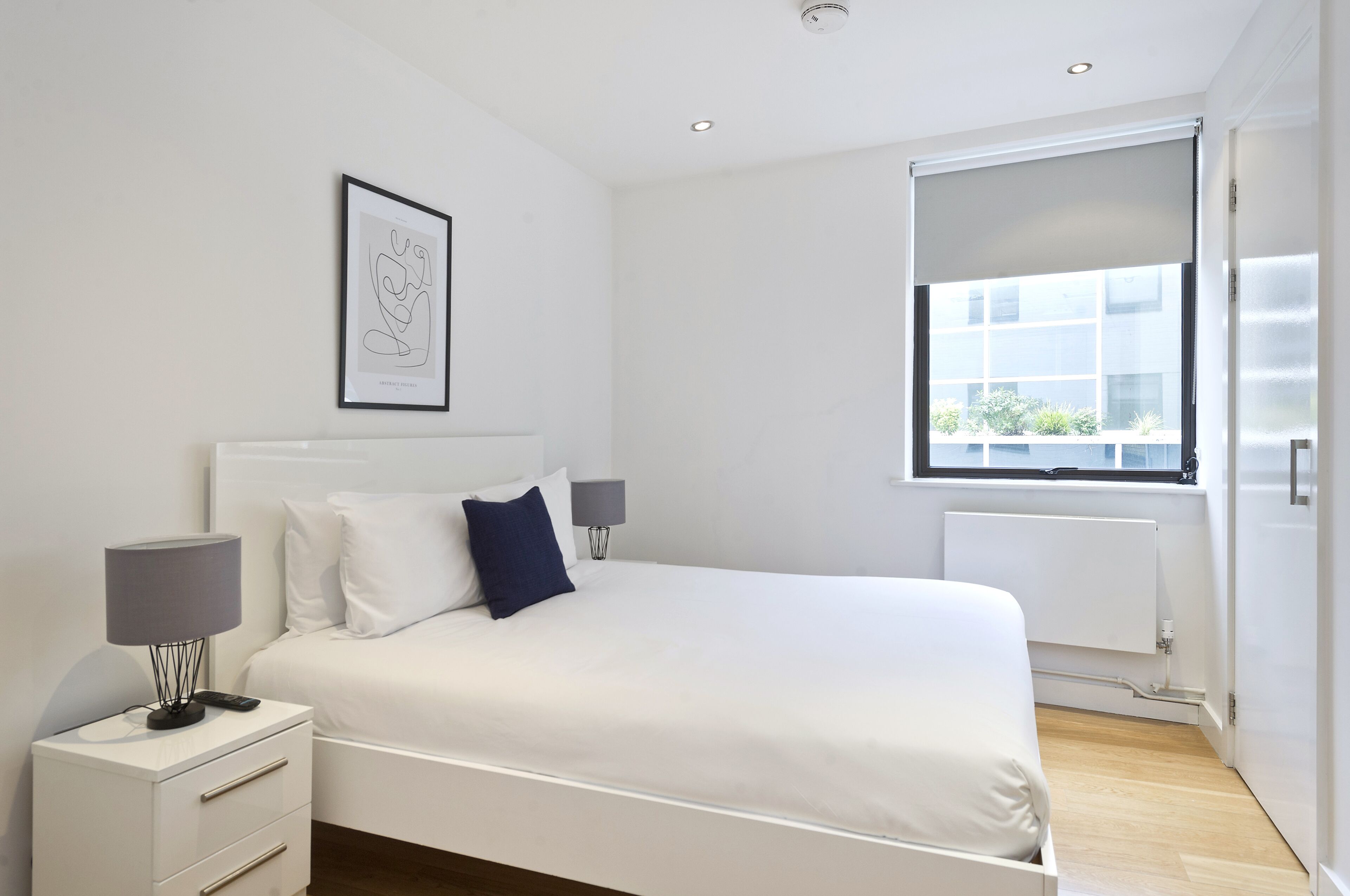 A modern bedroom with a large bed, bedside lamps, a framed artwork, and a window with a view.