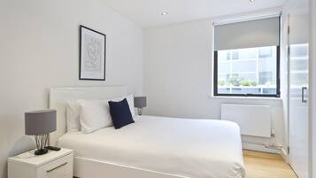 A modern bedroom with a large bed, bedside lamps, a framed artwork, and a window with a view.