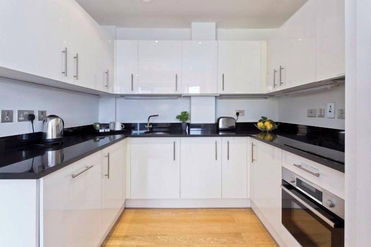 Una cocina moderna con armarios blancos, encimeras negras y electrodomésticos de acero inoxidable.