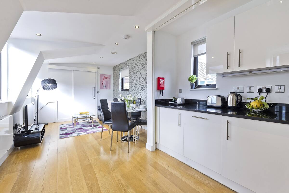 A modern kitchen with white cabinets, a black countertop, and a dining area with a table and chairs.