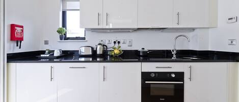 A modern kitchen with white cabinets, a black countertop, a Bosch dishwasher, and a window above the sink.