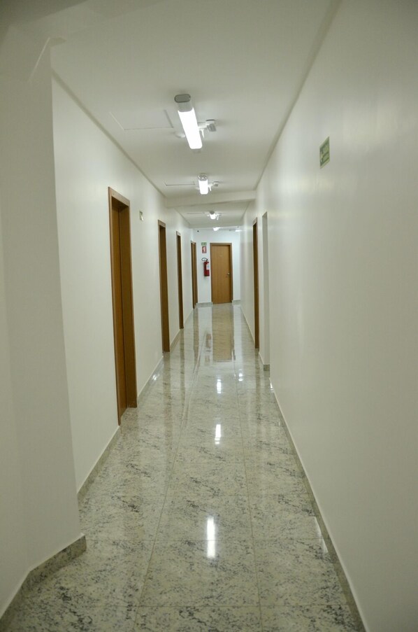 A long, narrow hallway with white walls and a polished marble floor. - Hotel JJ 44 (Goiania)