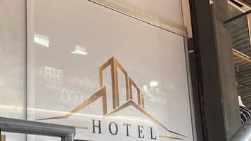 Entrada de hotel con fachada de vidrio, escalera de metal y una planta en primer plano.