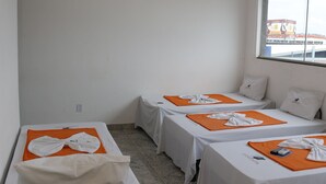 Ein Hotelzimmer mit zwei Einzelbetten, einem kleinen Tisch, einem an der Wand befestigten Fernseher und einem Fenster mit Blick ins Freie.