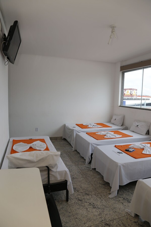 A hotel room with two single beds, a small table, a TV mounted on the wall, and a window with a view of the outside. - Hotel JJ 44 (Goiania)